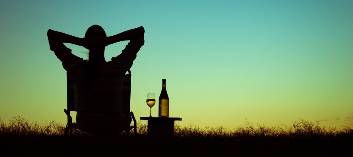 Mujer relajada en silla y tomando vino mientras ve un atardecer