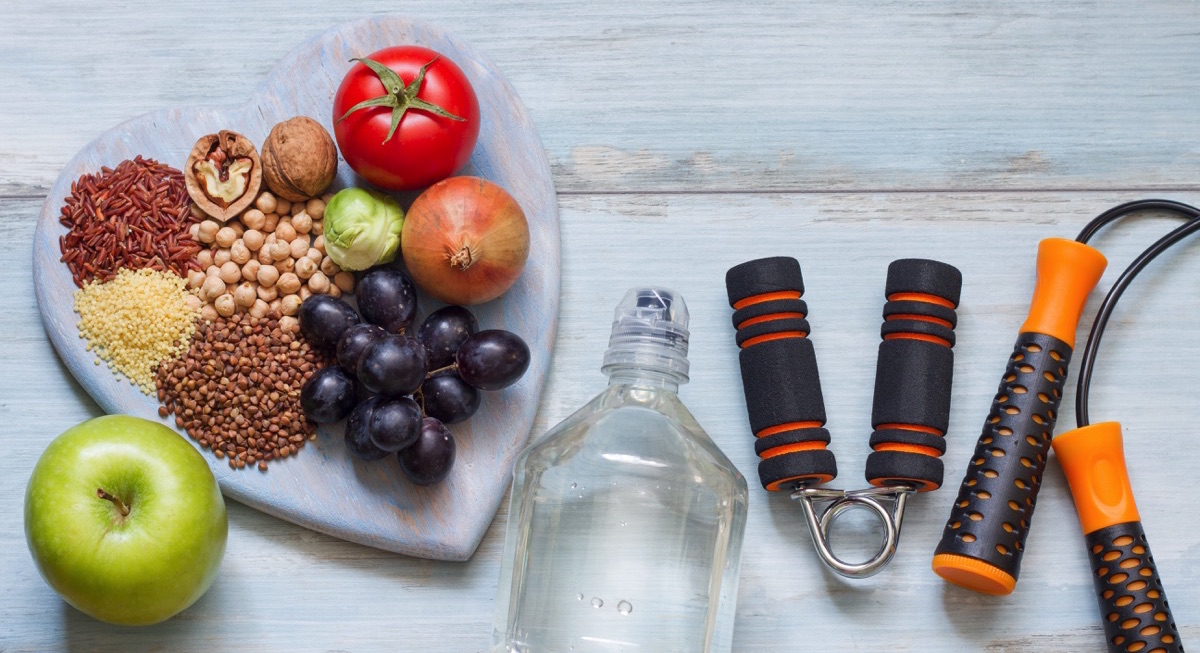 mesa con agua, pesas, cuerdas y comida saludable como frutas y verduras